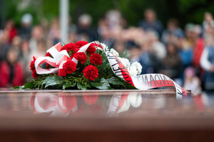 Na zdjęciu biało czerwone kwiaty złożone na pomniku z biało czerwona wstegą.