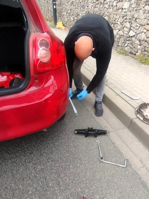 Policjant w cywilu podczas wymiany koła w samochodzie