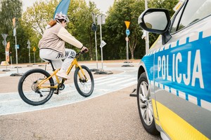 Na zdjęciu radiowóz policyjny i dziecko jadące rowerem.