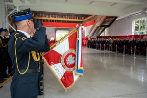 na pierwszym planie sztandar straży pożarnej, w tle uczestnicy uroczystości