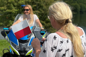 Zdjęcie przedstawia kobietę trzymającą flagę polski a w tle kobieta na policyjnym motocyklu