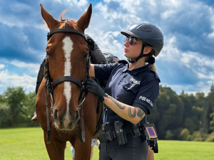Zdjęcie przedstawia policjantkę stojącą obok konia służbowego