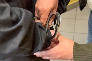 Zdjęcie przedstawia policjanta zakładającego mężczyźnie kajdanki na ręce trzymane z tyłu