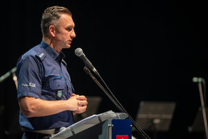 Zdjęcie przedstawia policjanta mówiącego do mikrofonu