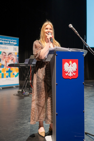 Zdjęcie przedstawia kobietę trzymającą mikrofon