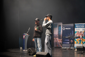 Zdjęcie przedstawia dwóch mężczyzn śpiewających na scenie do mikrofonów