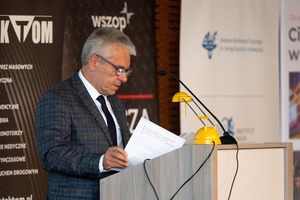 Zdjęcie przedstawia mężczyznę w garniturze przemawiającego podczas konferencji przy pulpicie z mikrofonem.