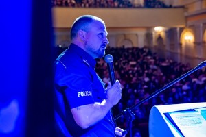 Zdjęcie przedstawia: umundurowanego policjanta, który przemawia.