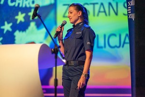 Zdjęcie przedstawia: policjantkę z mikrofonem podczas wypowiedzi.