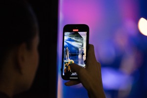 Zdjęcie przedstawia: telefon, którym ktoś fotografuje muzyków na scenie.