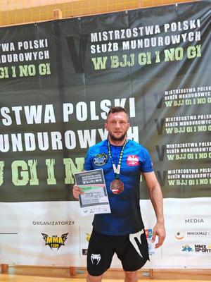 Zdjęcie przedstawia policjanta w stroju sportowym prezentującego medal oraz dyplom.