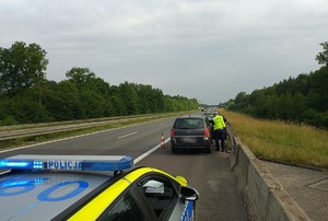 Zdjęcie przedstawia samochód osobowy oraz stojące przed nim i za nim oznakowane radiowozy policji. Przy pojeździe stoi umundurowany policjant.