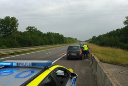 Zdjęcie przedstawia samochód osobowy oraz stojące przed nim i za nim oznakowane radiowozy policji. Przy pojeździe stoi umundurowany policjant.