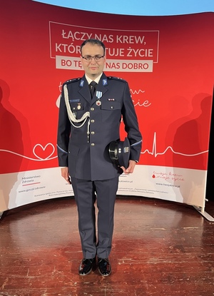 zdjęcie przedstawia sylwetkę asp. Maksymiliana Stachura na tle plakatu "łączy nas krew, które ratuje życie"