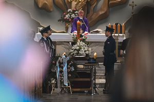 grafika przedstawia trumnę wraz z asystą honorową oraz kapłanem odparwiającym cerelonię pogrzebową