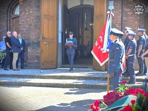zdjęcie przedstawia funkcjonariusza kompani honorowej, który wychodzi z kościoła niosąc w rękach czapkę garnizonową aspiranta sztabowego
