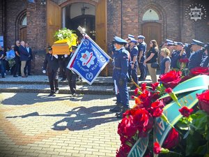 zdjęcie przedstawia trumnę w obecności sztandaru Komendy Powiatowej Policji w Będzinie oraz funkcjonariuszy policji na tle kościoła
