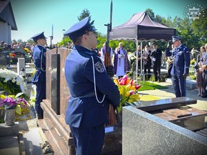 zdjęcie przedstawia policjantów asysty honorowej oraz oficera policji, który oddaje honory na cmentarzu