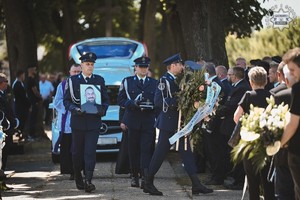 grafika przedstawia policjantów kompani honorowej na cmentarzu , którzy niosą zdjęcie zmarłego oraz czapkę podoficera