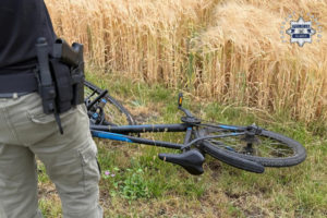 na zdjęciu fragment osoby z bronią przy leżącym rowerze