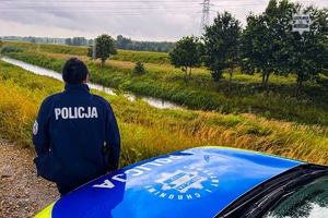 Zdjęcie przedstawia policjantkę stojącą przy oznakowanym radiowozie i monitorującą stan rzek.