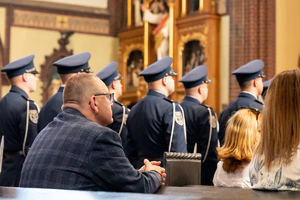 kolorowe zdjęcie z profilu mężczyzny ubranego w marynarkę, w tle stoją policjanci kompani hoorowej.