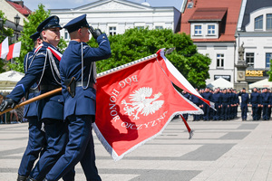 kolorowe zdjęcie przedstawiające policjantów maszerujących ze sztandarem
