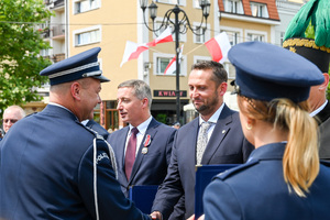 kolorowe zdjęcie przedstawiające Oficera Policji wręczającego odznaczenia gościom honorowym obchodów Święta Policji