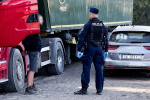 Na zdjęciu mężczyzna z założonymi kajdankami stoi obok tira, obok stoi policjant