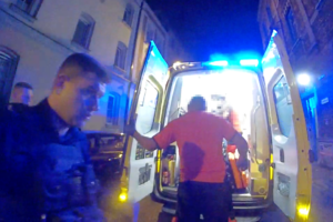 Na zdjęciu widnieje funkcjonariusz Policji, a obok niego wchodzącego mężczyznę do pojazdu zespołu ratownictwa medycznego.