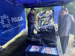 Na zdjęciu widoczne jest policyjne stoisko z policyjnym wyposażeniem, któremu przygląda się grupa osób.