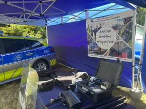 Na zdjęciu widoczny jest oznakowany radiowóz policyjny, a obok niego na stoliku znajduje się wyposażenie Policji.