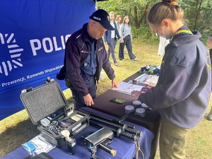 Na zdjęciu widoczne jest policyjne stoisko z policyjnym wyposażeniem, któremu przygląda się grupa osób.