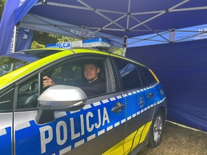 Na zdjęciu widoczny jest oznakowany radiowóz policyjny, za kierownicą którego znajduje się osoba.