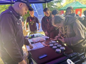 Na zdjęciu widoczne jest policyjne stoisko z policyjnym wyposażeniem, któremu przygląda się grupa osób.