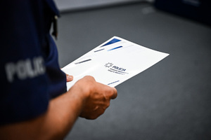 Na zdjęciu widoczna jest teczka z napisem: Policja Komenda Wojewódzka Policji w Katowicach, którą trzyma umundurowany funkcjonariusz Policji.