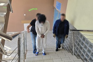 na zdjęciu widać dwóch policjantów wydziału kryminalnego prowadzącego podejrzanego po schodach, który ma ubrane kajdanki zespolone