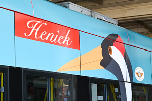 Na zdjęciu widać górną część niebieskiego tramwaju, na którym umieszczony jest napis &quot;Heniek&quot;, a obok niego namalowany jest żuraw.