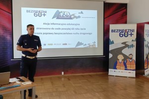 Na zdjęciu widoczny jest umundurowany funkcjonariusz Policji, który prowadzi akcję informacyjno-edukacyjną związaną z bezpieczeństwem seniorów.