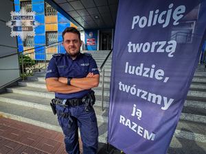 Na zdjęciu widoczny jest umundurowany funkcjonariusz Zespołu Prasowego Komendy Wojewódzkiej Policji w Katowicach, który stoi przed wejściem do jednostki Policji.