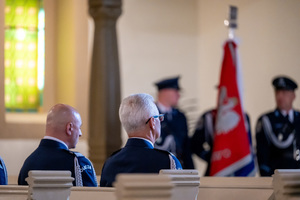 policjanci w mundurach galowych siedzą w ławie kościelnej, w tle poczet sztandarowy