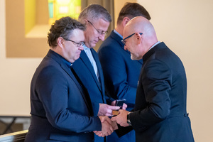 mężczyzna w garniturze wręcza medal księdzu