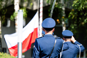 policjanci w strojach galowych wciągają flagę biało czerwoną na maszt