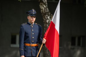 chłopak w historycznym mundurze trzyma biało czerwoną flagę