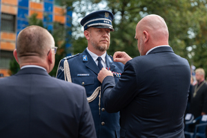 mężczyzna w garniturze przypina medal policjantowi w mundurze galowym