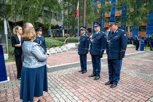 trzech policjantów w mundurach galowych stoi przed kobietą i mężczyzną w garniturze