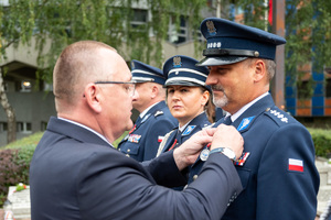 mężczyzna w garniturze wręcza medal policjantowi w mundurze galowym