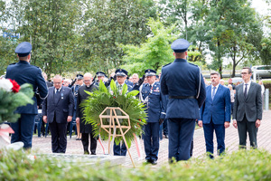 Komendanci  w mundurach galowych wraz z duchownymi oraz mężczyznami w garniturach składają wieniec w miejscu pamięci