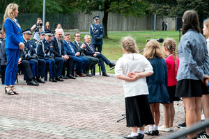grupa dzieci występuje przed publicznością, wśród której są policjanci w mundurach galowych