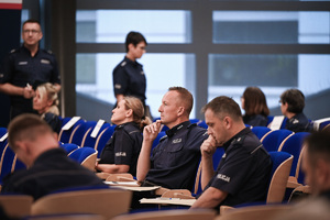 umundurowani policjanci i policjantki siedzą na krzesłach w auli